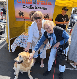 Two women with golden retriever at booth.