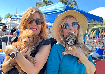 Two women holding doodle puppies.